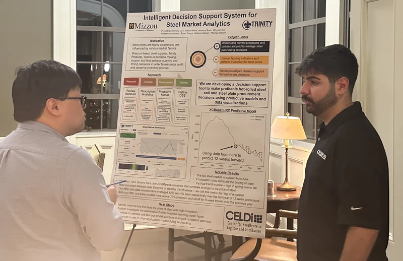 PhD student Pyam Oveys discussing steel-market decision-support research beside a Trinity Products project poster.